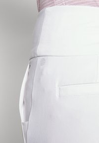 Vita byxor med en slät textur, utrustade med en sidficka, bakficka och en subtil logodetalj nära midjan.