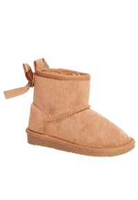 Stivale in suede color nocciola con punta arrotondata, altezza corta e dettaglio con nastro sul retro. Presenta una suola testurizzata e accenti di cuciture.