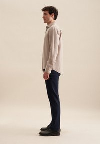 Lichtbeige longsleeve shirt van linnen, gecombineerd met marineblauwe broeken en zwarte schoenen. Eenvoudige knopen en een relaxte pasvorm opgemerkt.