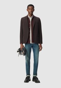 Czarna marynarka noszona na bordowej koszuli, jasna szalik w kratę w ręku, w połączeniu z niebieskimi dżinsami i czarnymi butami. Prosty, dopasowany fason.