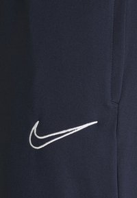 Marineblauwe Nike-sweatpants met een zachte textuur, voorzien van een opvallend wit geborduurd swoosh-logo aan de linkerkant.