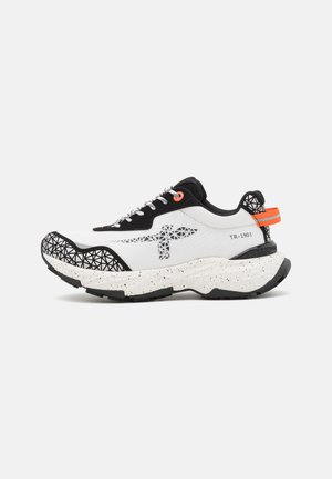 Zapatilla con una parte superior blanca y acentos negros, patrón geométrico en la puntera, detalles naranjas y una entresuela blanca moteada.