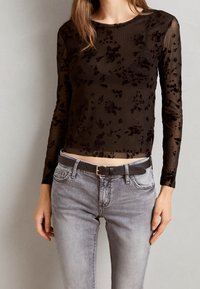 Svart genomskinlig långärmad topp med blommönster; matchad med ljusgrå denimjeans och ett svart bälte. Mjuk textur med ribbat mönster.