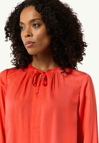 Czerwona jedwabna bluzka z marszczonym dekoltem, detalem do wiązania i długimi rękawami. Gładka faktura z delikatnym połyskiem.
