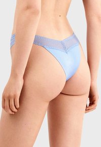 Tanga azul claro con una cinturilla de encaje. Textura suave y cobertura mínima, con un delicado patrón de encaje a lo largo del borde superior.