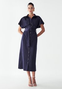 Tumesinine triibuline midi kleit lühikeste varrukatega, vööga taljes ja kahe esiosa taskuga. Omab nööpkinni sulgemist ja lõdva istuvust.