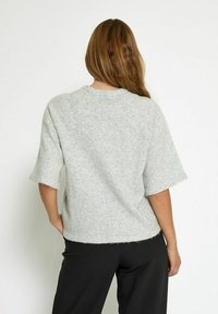 Gray textured sweater with short sleeves, featuring a relaxed fit and raw edge hems. Worn with black pants, viewed from the back.