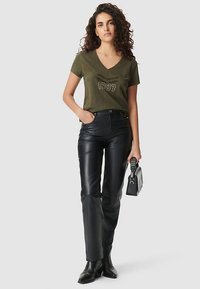 Oliwkowozielona koszulka z dekoltem w serek z nadrukiem '1987' w białym kolorze, zestawiona z wysokim stanem czarnych skórzanych spodni i botków za kostkę. Do kompletu mała czarna torebka.