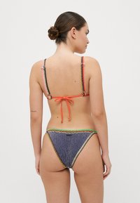 Bikini-Set mit mehrfarbigen Trägern, Bindebändern am Rücken und einem strukturierten blauen Bottom mit kontrastierenden dekorativen Nähten.