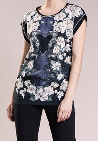 Top de manga corta con estampado floral que presenta un fondo oscuro, intrincados patrones botánicos y un acabado ribeteado alrededor del escote.