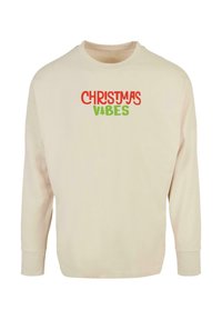 Krém színű, hosszú ujjú pulóver, amelyen piros és zöld színű "CHRISTMAS VIBES" felirat található. Puha anyagból készült, laza szabással és bordázott mandzsettákkal.