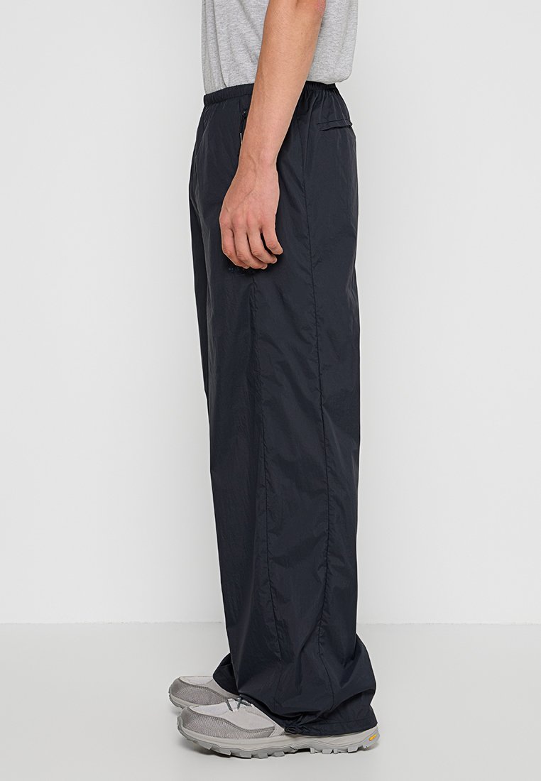 Zwarte, lichte broeken met elastische tailleband, zijzakken, gladde textuur en recht gesneden ontwerp, gedragen met grijze schoenen.