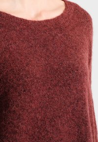 Bordeaux stickad tröja med en mjuk, fluffig textur och en rundad halsringning, med en avkopplad passform och minimal detaljering.