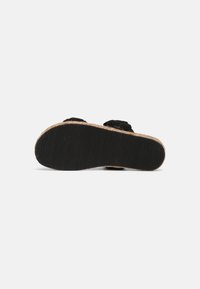 Sandale en tissu noir avec une semelle texturée et un bord en jute tressé. La partie inférieure présente un motif noir nervuré pour une meilleure adhérence.