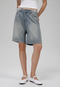 Denim šorti ar gaiši zilu krāsu, kurām ir piecu kabatu dizains, izšūta apmale un pogu aizdare jostasvietā.