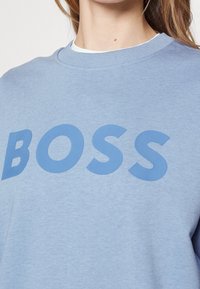 Il sudario azzurro chiaro presenta un collo a coste, una texture morbida e un audace logo "BOSS" in blu scuro sul davanti.