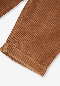 Braunes Cordstoffgewebe mit schmalen, vertikalen Rippen. Verfügt über eine gesäumte Kante mit einer gerippten Textur. Weiches und dickes Material, geeignet für Bekleidung.