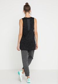 Top nero senza maniche con un motivo floreale texturizzato e tre strisce verticali grigie sul retro, abbinato a joggers grigi e sneakers bianche.