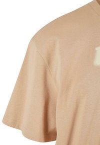 Short-sleeve, beige cotton t-shirt with a round neckline and soft texture. Features subtle stitching detail on sleeves and hem.