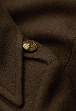 Brauner Wollmantel mit strukturierter Stoffoberfläche, ausgestattet mit einem goldenen Knopf am Kragen und scharfen Revers, der das maßgeschneiderte Design hervorhebt.