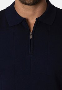 Polo de color azul marino con cremallera y una textura suave, con un cuello clásico y detalles de costura vertical. El tirador de la cremallera es de tono plateado.