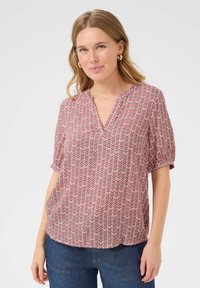 Blouse à manches courtes rose avec un motif en zigzag rouge et bleu marine, dotée d'un col en V et d'une coupe ample, fabriquée en tissu léger.