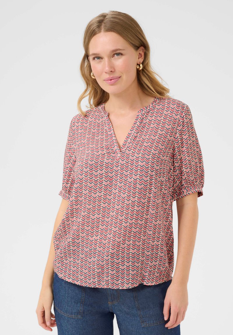 Blouse à manches courtes rose avec un motif en zigzag rouge et bleu marine, dotée d'un col en V et d'une coupe ample, fabriquée en tissu léger.