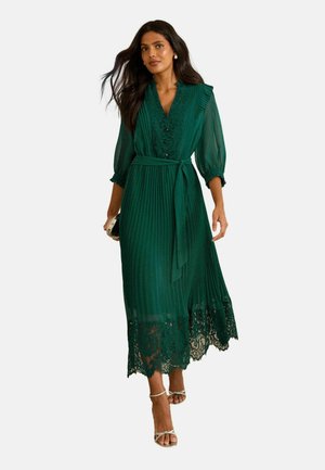 Emerald green pleated dress with a V-neck, lace trim at the hem, and a matching belt. Sheer sleeves and textured fabric enhance detail.