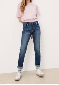 Ljust rosa kort t-shirt med samlad midja; mörkblå slim-fit jeans; vita sneakers med rosa sulor; synliga uppvikta ärmar och randiga strumpor.