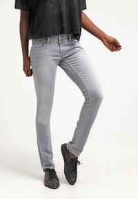 Jeans skinny de denim gris claro con diseño de cinco bolsillos, costuras en contraste y textura ligeramente desgastada. Llevados con zapatillas negras con cordones.