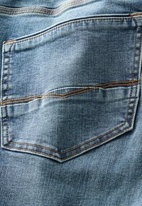 Blauwe denimstof met een gestikte, schuine achterzak. De zak heeft oranje draadaccenten en een gestructureerd oppervlak.