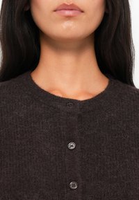 Dark brown cardigan made of soft, fuzzy material with a round neck and front button closure featuring four gray buttons.