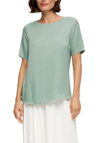 Hellgrünes Kurzarm-Bluse aus einem glatten, fließenden Stoff mit Rundhalsausschnitt, leicht längerem Rückensaum und minimalen Nähedetails.