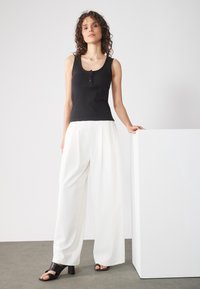 Black ribbed tank top with button detail, paired with white wide-leg trousers and black heeled sandals. Simple, well-defined shapes and textures.