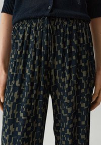 Pantalons noirs à motifs fabriqués en tissu léger, dotés d'une taille élastique avec cordon de serrage et de motifs géométriques verts olive sur tout le matériau.