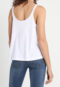 Débardeur blanc en coton avec larges bretelles et encolure arrondie, associé à un jean bleu avec une coupe classique à cinq poches.