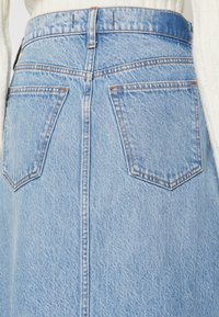 Gonna di jeans azzurro chiaro con tasche posteriori e cuciture in evidenza, indossata con un top bianco lavorato a maglia.