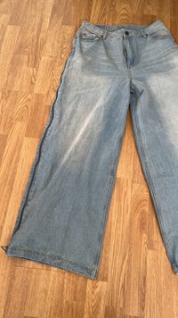Jeans largos de ganga azul clara com um acabamento desbotado, cinco bolsos e fecho com botão. Barra reta com detalhes de costura visíveis.