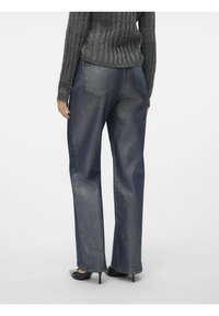 Jeans in denim scuro a gamba larga con leggero lucido, dotati di tasche posteriori e orli sfrangiati, abbinati a un maglione aderente grigio a costine.