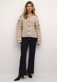 Cardigan a maglia grossa in beige e crema con strisce orizzontali, dotato di grandi bottoni, polsini a coste e una silhouette morbida.