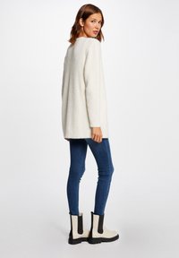 Vit, fluffig tröja med rundad halsringning, långa ärmar och en lös passform, kombinerad med blanka jeans och svartvita ankelstövlar.