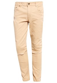 Jeans slim-fit beige con strappi sulle cosce e orli sfrangiati appena sotto il ginocchio, dotati di tasche frontali e chiusura a bottone.
