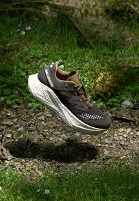 Brown athletic shoe with a mesh upper, contrasting white midsole, and textured outsole. Features logo and ventilation holes.