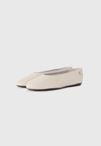Beiga läder slip-on platta skor med svarta sulor, rundade tår och en liten metallisk logotyp på hälkappan.