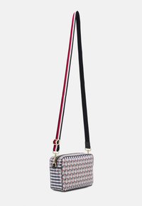 Rektangulær crossbody taske lavet af stof med røde, blå og hvide geometriske mønstre. Har en gylden lynlås og en tyk, stribet justerbar rem.