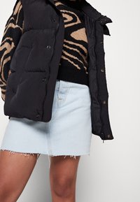 Svart puffert vest med dragkedja framtill, bärs över en zebra-mönstrad tröja, ihop med en ljus denim minikjol med franskant.