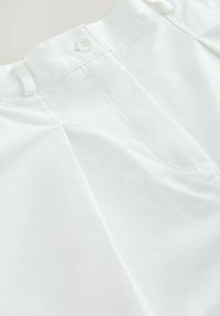 Pantalons en coton blanc avec fermeture à bouton, façade plate et détails de couture subtils. Texture lisse et coupe ajustée.