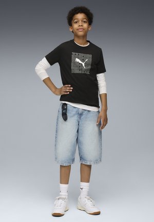 Zwarte korte mouwen t-shirt met witte lange mouwen eronder, spijkerbroekshorts en witte sneakers. Logo op het t-shirt; zonnebril op de shorts.