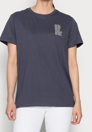 Osoba ubrana w ciemnoszary jednolity T-shirt z białym, motywacyjnym napisem na lewej piersi oraz białe spodnie.