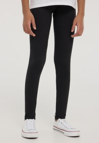 Czarne legginsy wykonane z elastycznej tkaniny, dopasowany krój, gładka tekstura, z elastycznym paskiem u góry, w połączeniu z białymi trampkami.